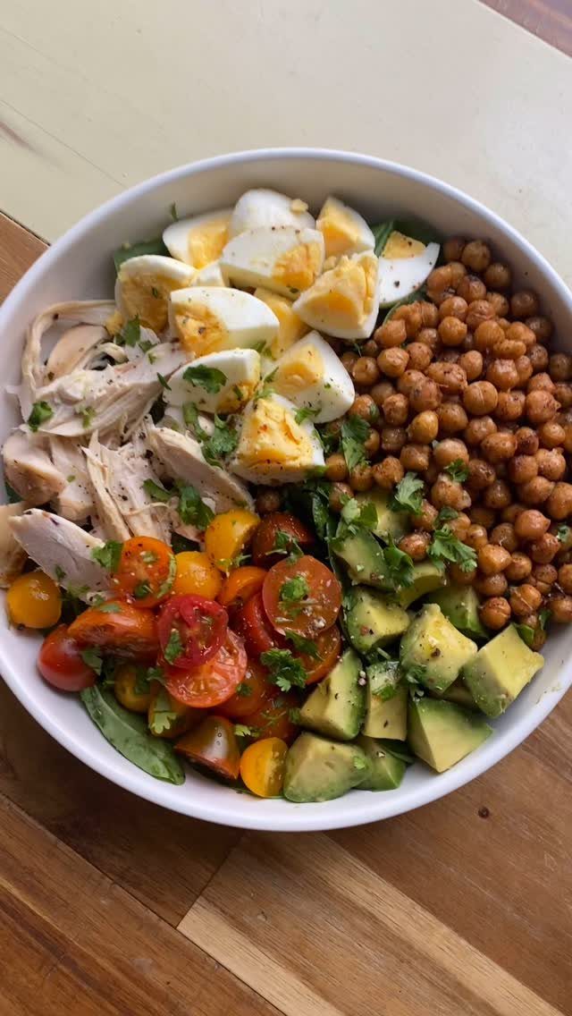 Healthy food bowl with eggs, chicken, chickpeas, tomatoes, and avocado on wood.