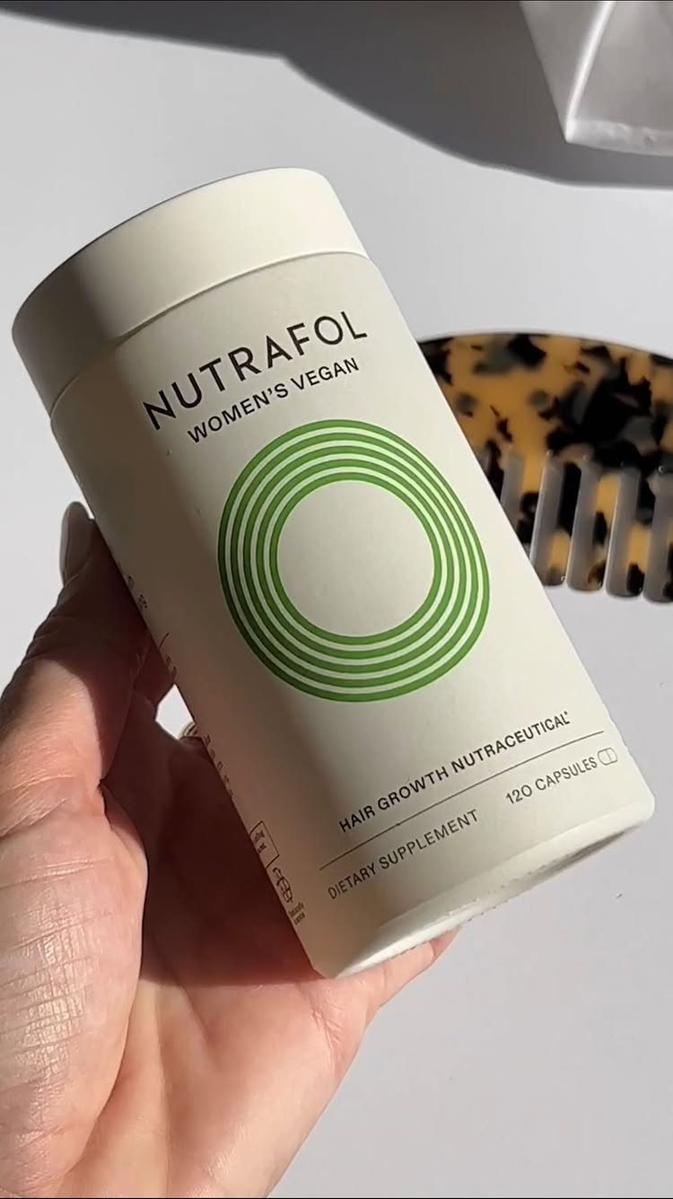 Nutrafol hair growth supplement bottle held in a hand next to a comb.