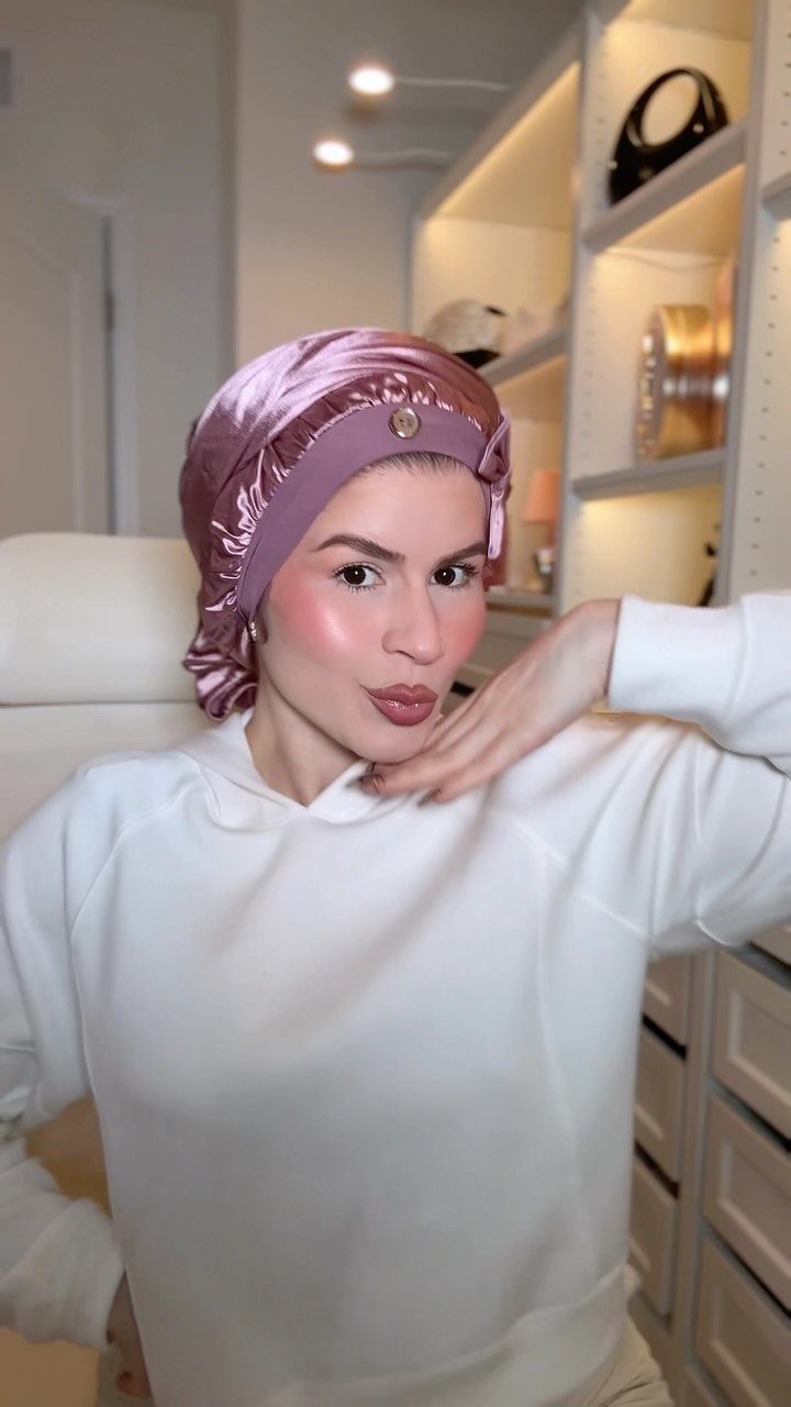 Woman wearing a pink satin hair bonnet and a white sweatshirt.