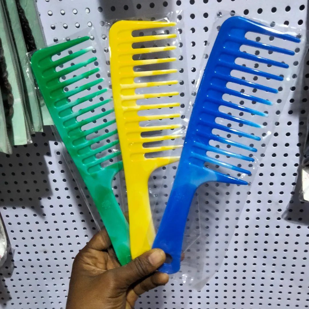 Three colorful wide-tooth combs in green, yellow, and blue held by a hand.