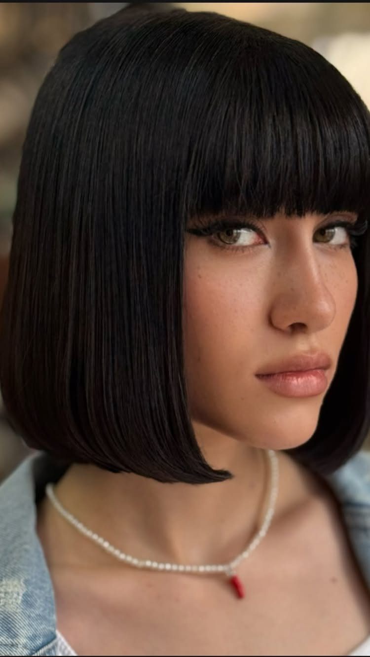 Woman with a black bob and straight blunt cut bangs wearing a pearl necklace.