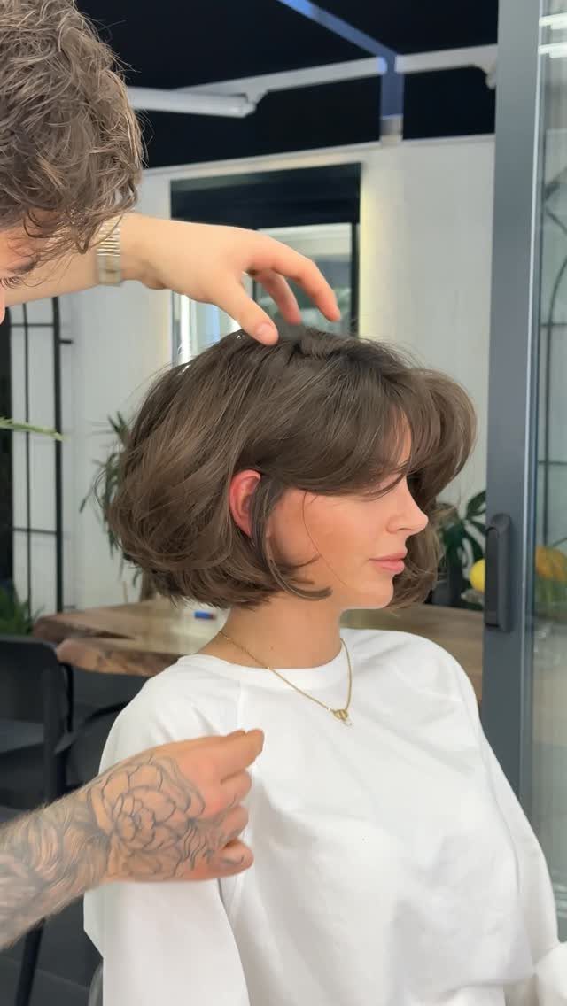 Woman with a brown bob and bangs being styled by a hairdresser.