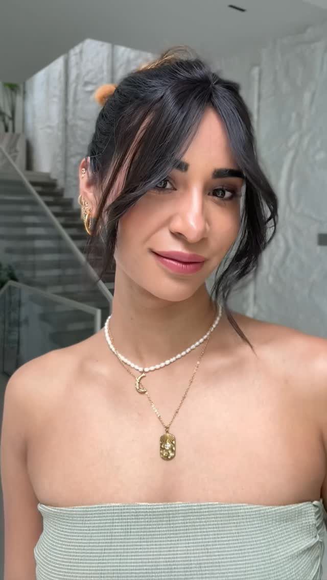Woman with dark hair and center-parted curtain bangs wearing a strapless green top.