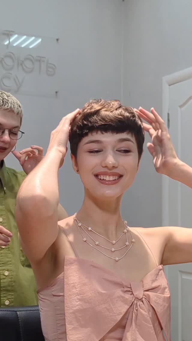 Woman with a brown pixie cut and short textured bangs smiling and posing.