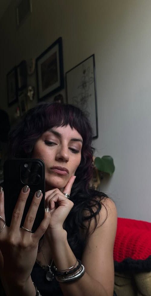 Woman with dark purple hair and short choppy bangs taking a mirror selfie.