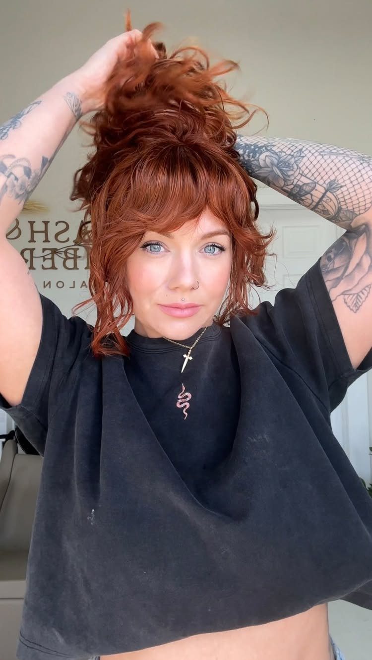 Woman with red hair featuring wavy bangs and a high messy bun.