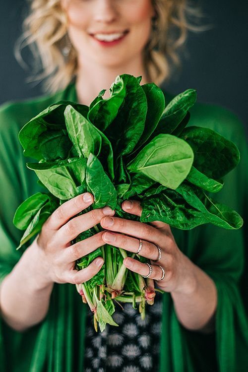 Fresh green spinach leaves held by a person wearing a green garment.