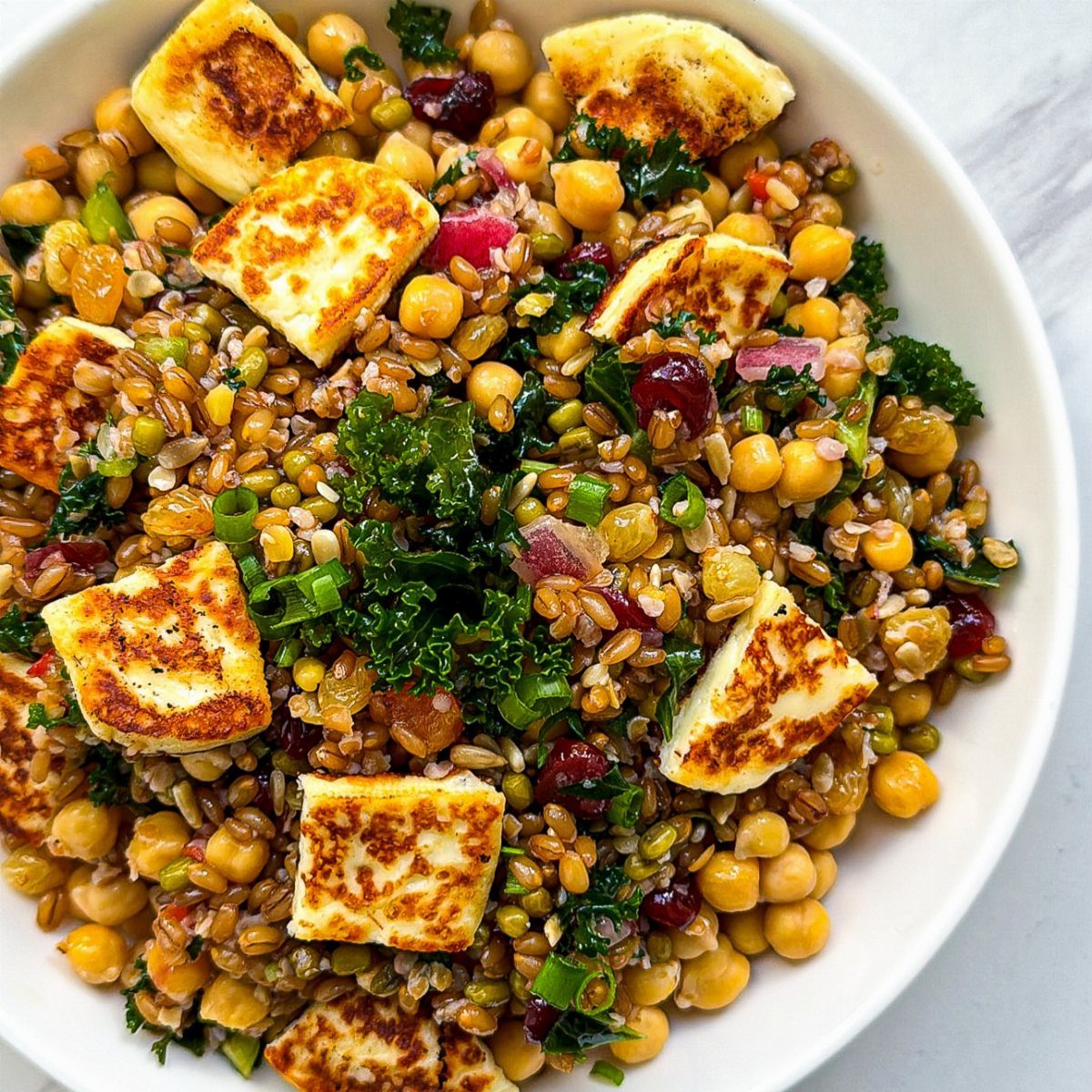 Chickpea and grain salad with kale and seared halloumi cheese in a white bowl.
