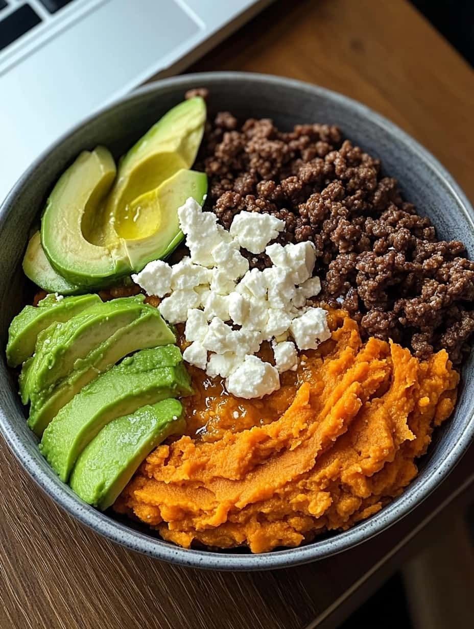Bowl of ground meat, avocado, sweet potato, and cheese on a wooden table.