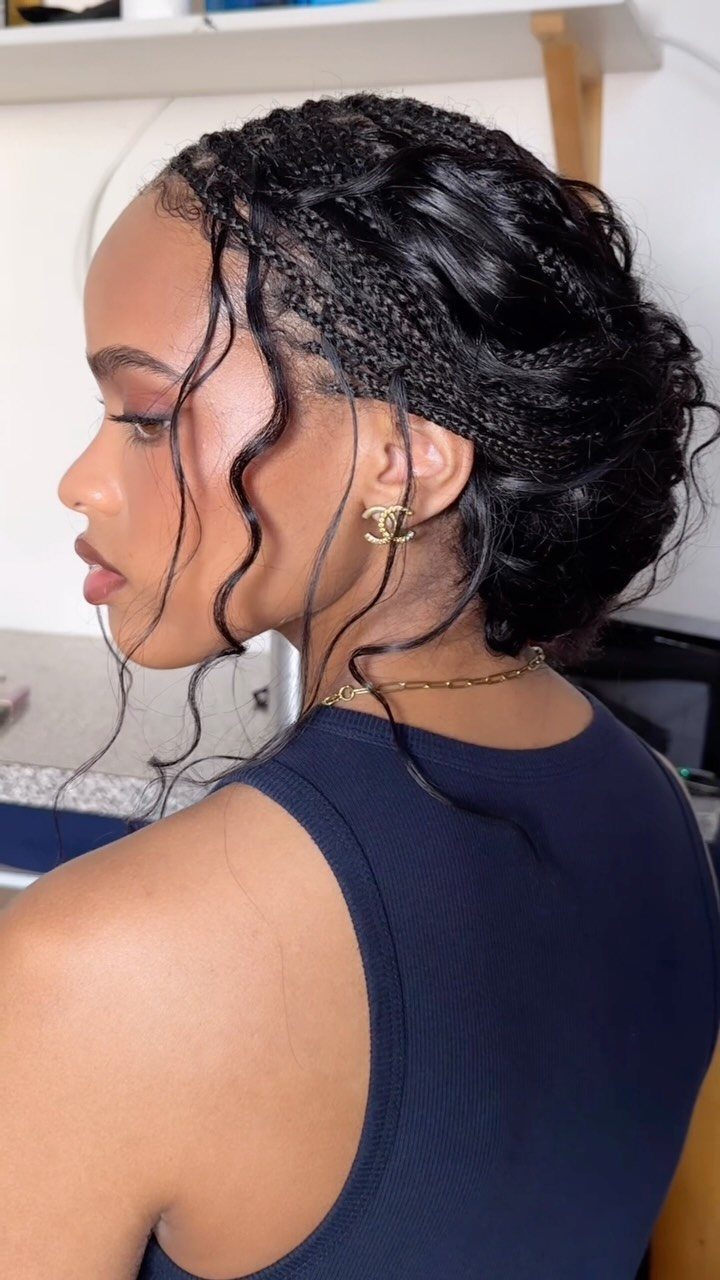 Woman with black hair in a braided updo with loose curly tendrils.