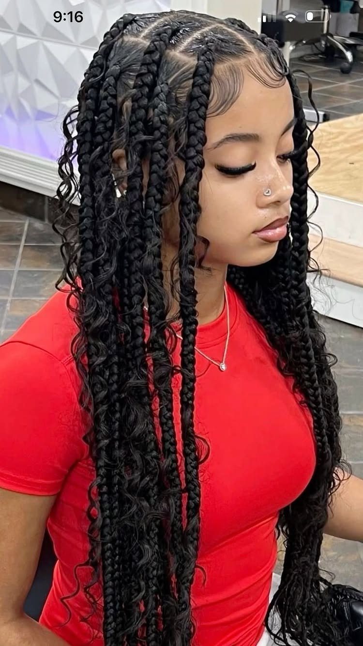Woman with long black box braids and curly ends wearing a red shirt.
