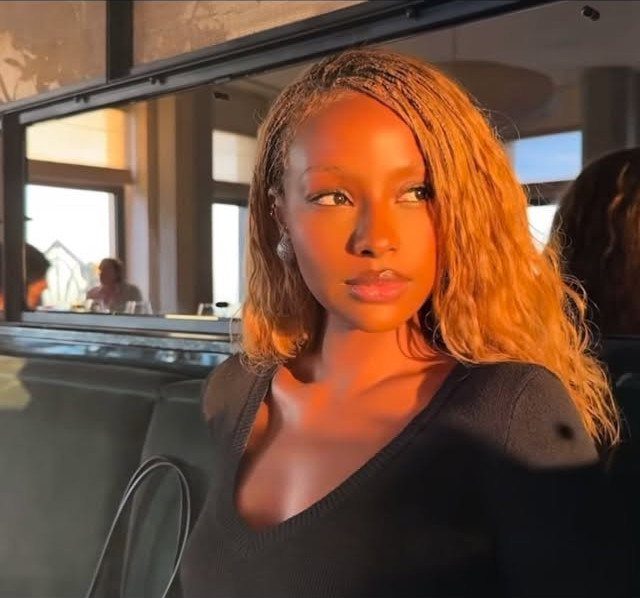 Woman with long, fine golden-brown micro braids wearing a black V-neck top.
