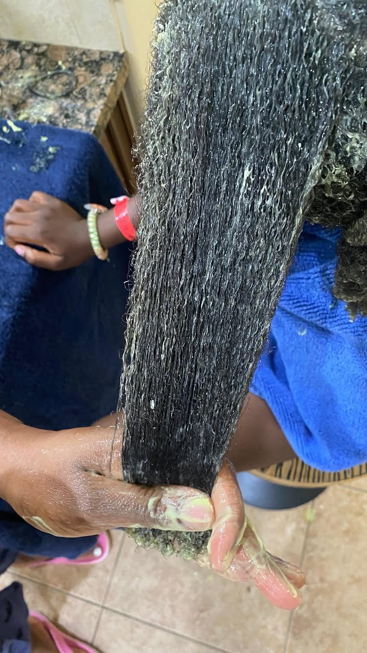 Hands applying thick white conditioner to a section of dark coiled 4c hair