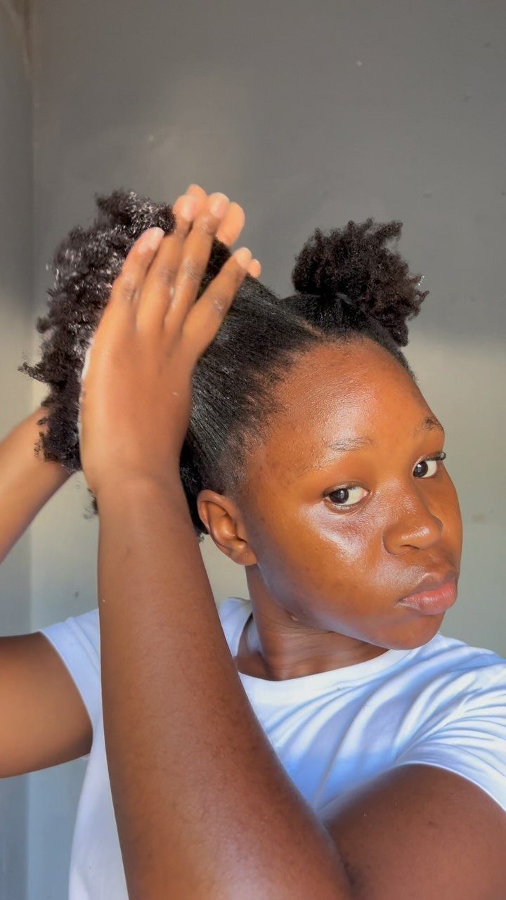 Young Black woman with 4C hair using fingers to detangle her hair puffs.