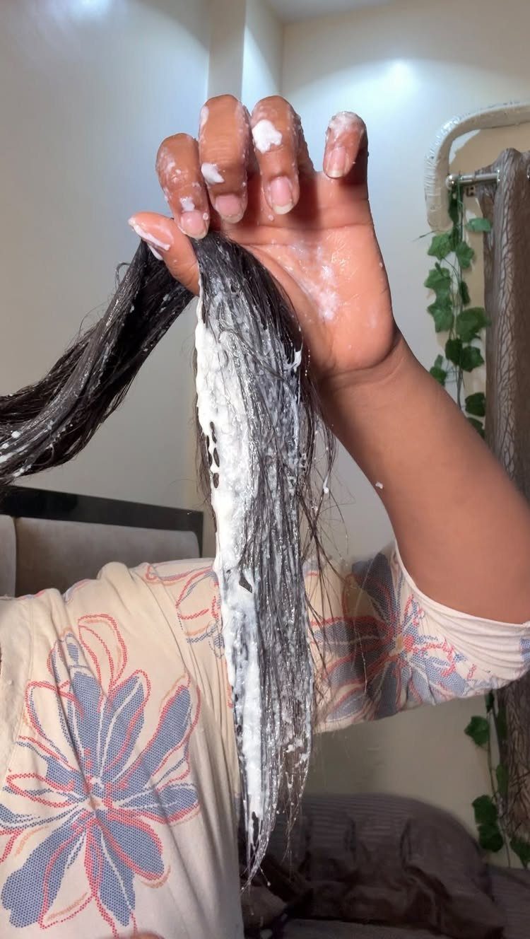 Hand applying white hair conditioner to long dark hair in an indoor setting