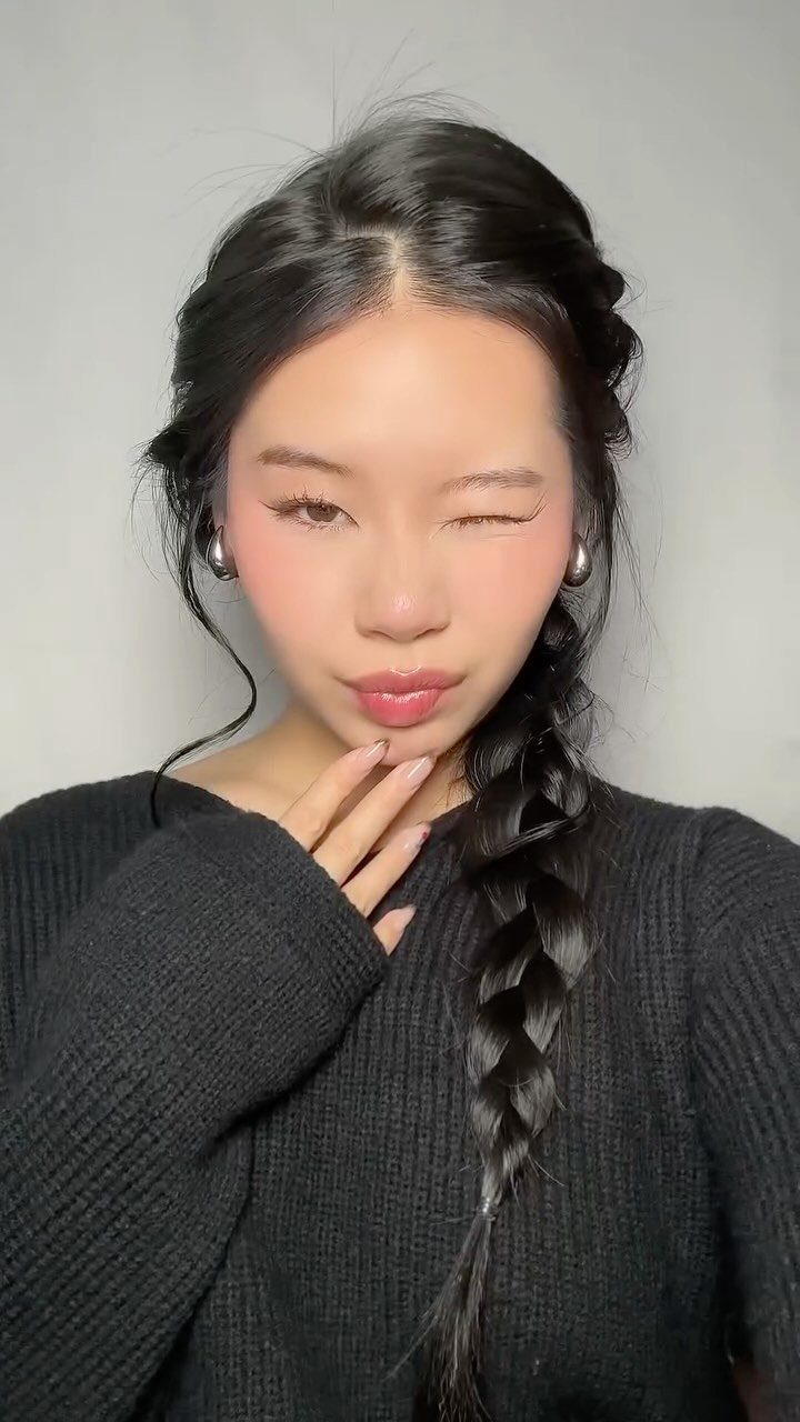 Woman with long black hair styled in a side braid and black sweater.