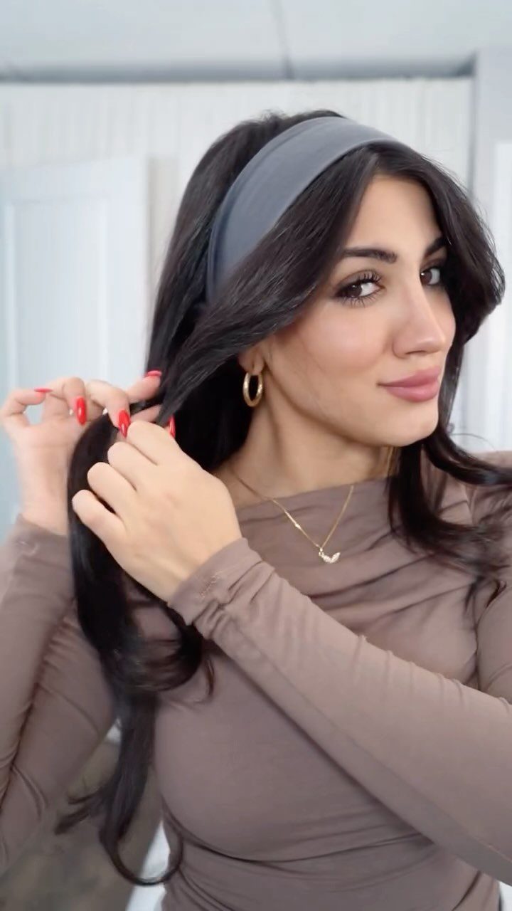 Woman with long dark wavy hair wearing a grey fabric headband and brown top.
