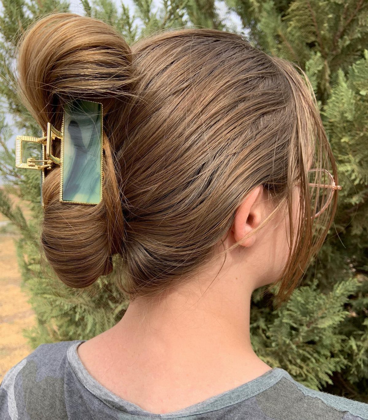 Brown hair styled in a high bun secured with a green claw clip.