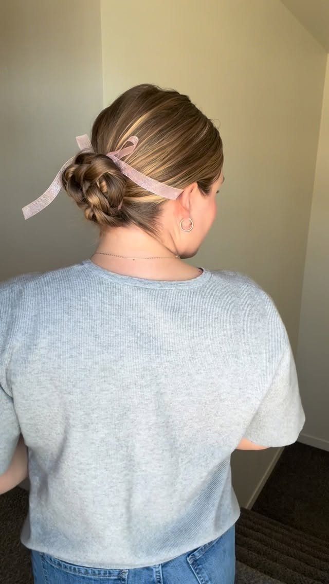 Woman with brown hair in a braided low bun tied with a pink bow.