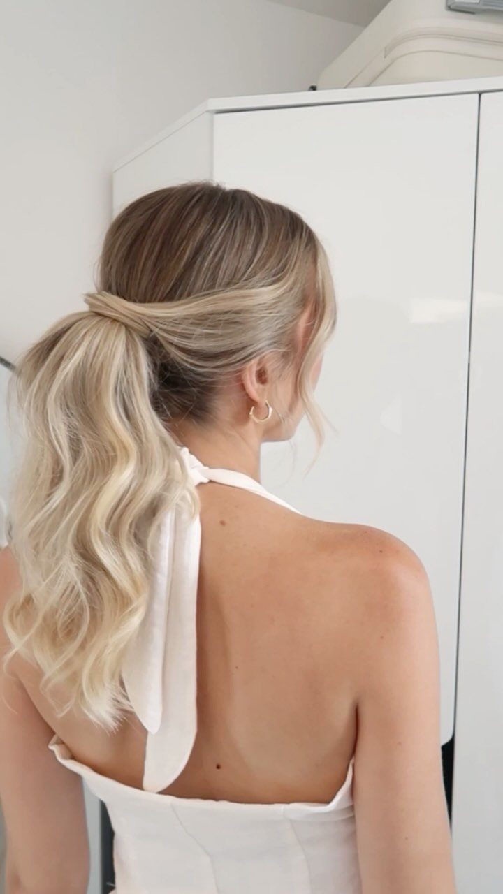 Blonde woman with a voluminous low ponytail wearing a white halter top.
