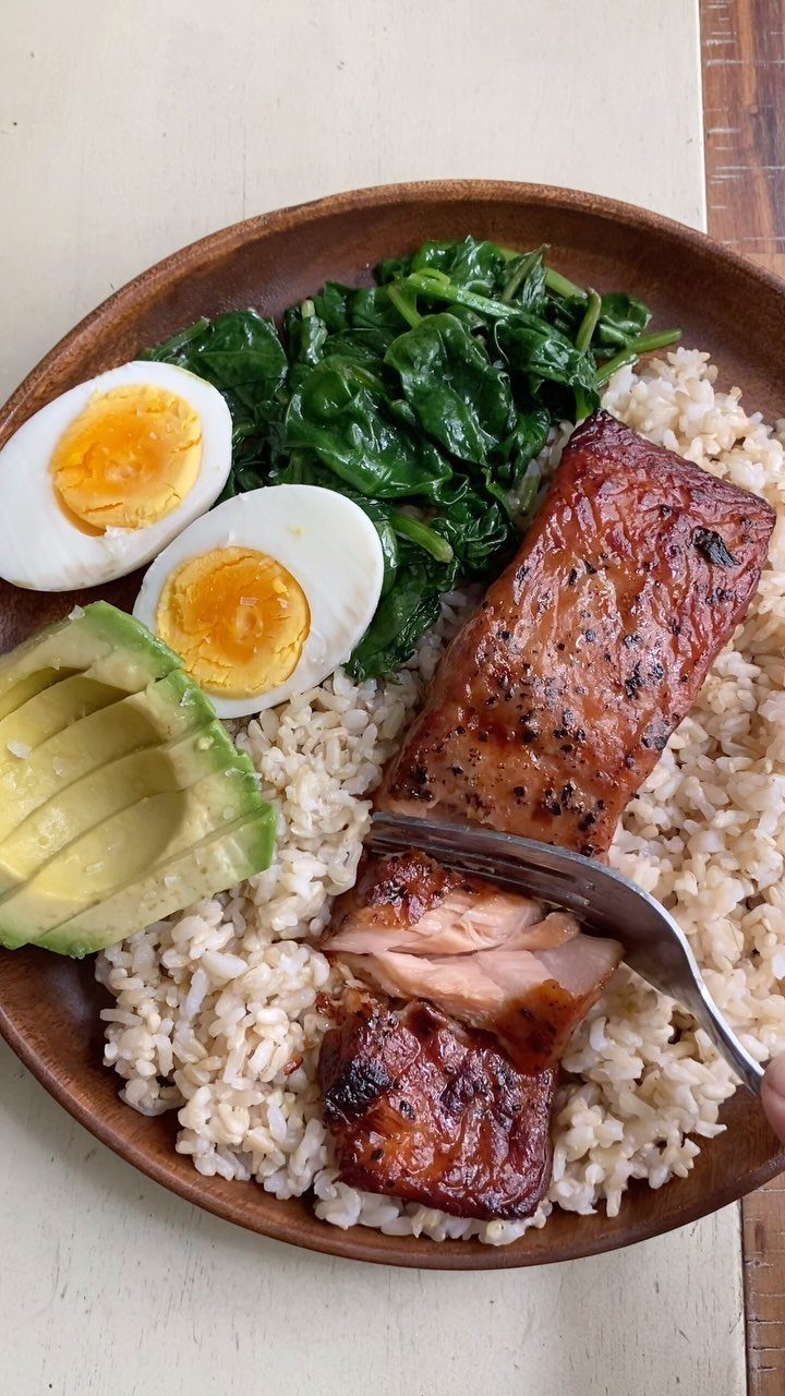 Grilled salmon fillet on brown rice with spinach, boiled eggs, and avocado slices.