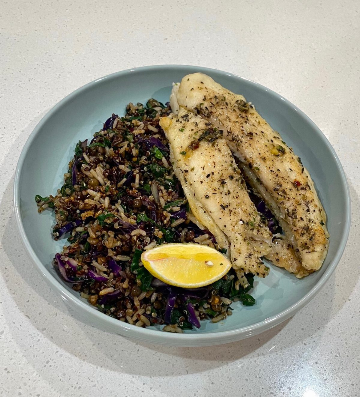 Grilled chicken breast with brown rice, purple cabbage, and a lemon wedge in a bowl.