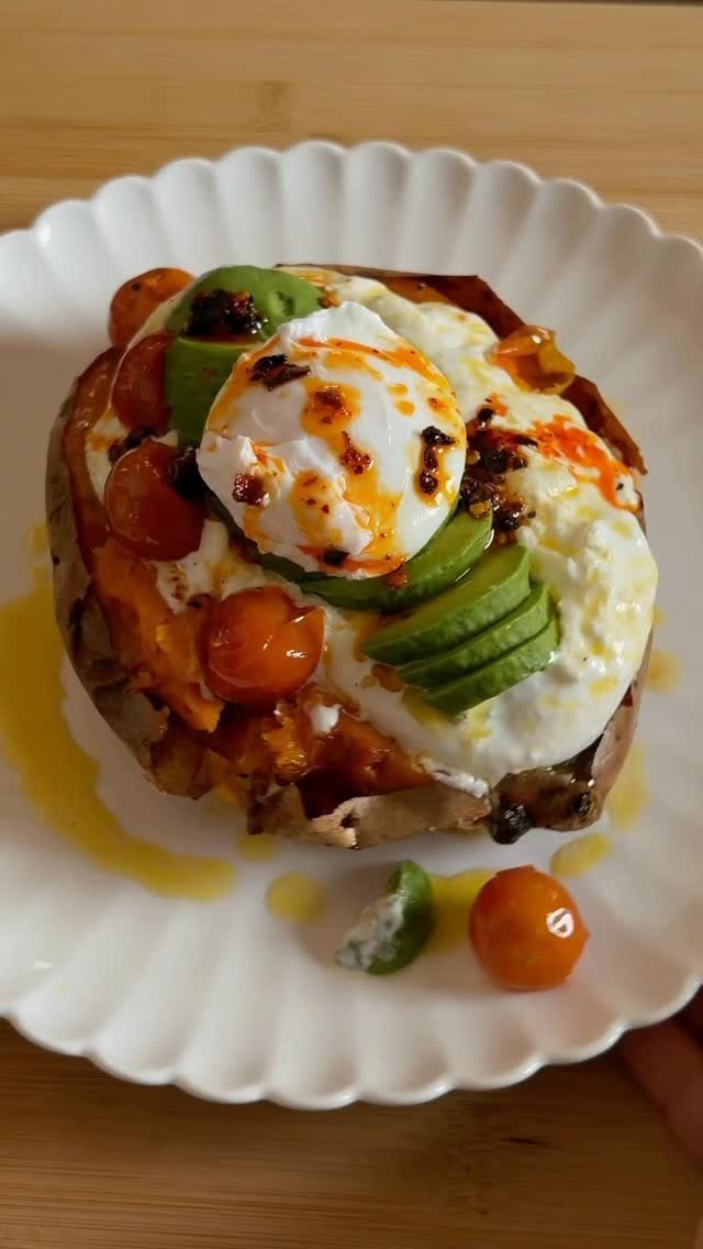 Baked sweet potato topped with poached egg, avocado slices, and cherry tomatoes on a plate.