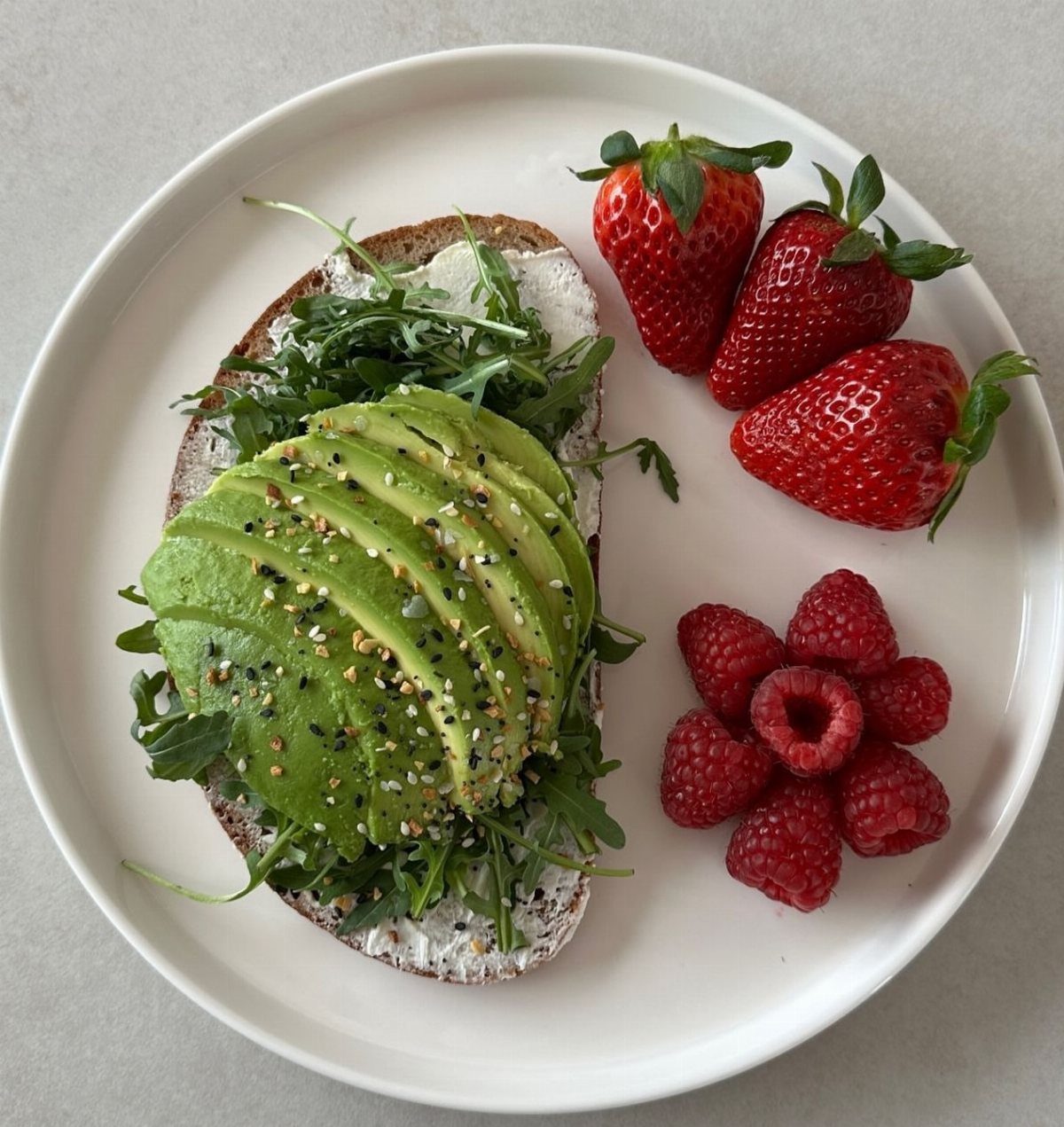 Avocado toast with arugula, strawberries, and raspberries on a white plate.