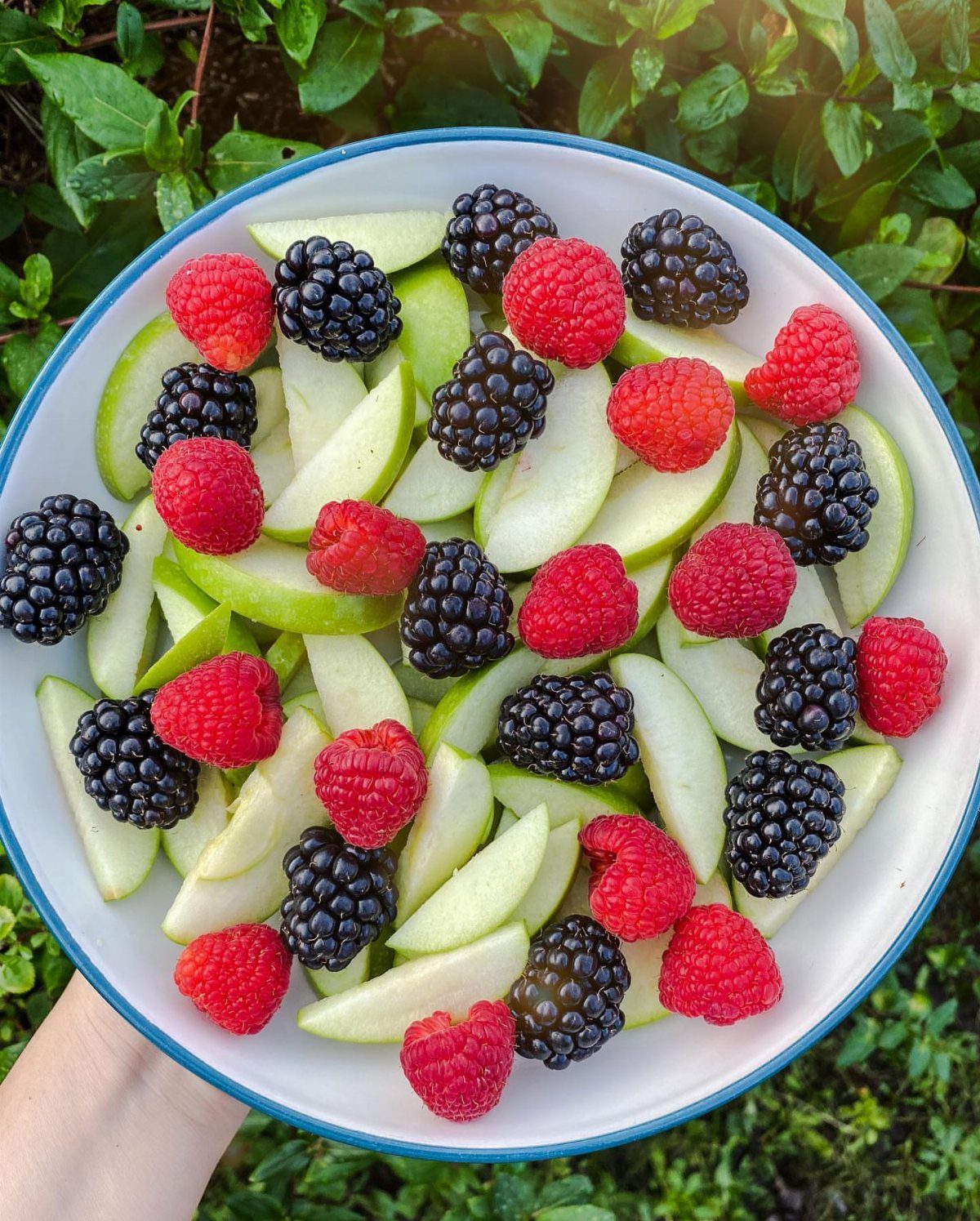 Sliced green apples mixed with red raspberries and blackberries in a white bowl.