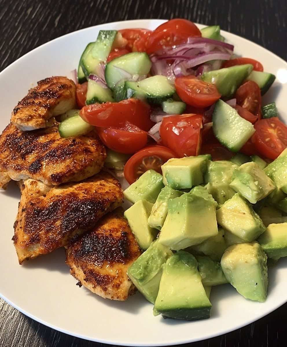 Grilled chicken breast served with diced avocado and a fresh tomato cucumber salad.