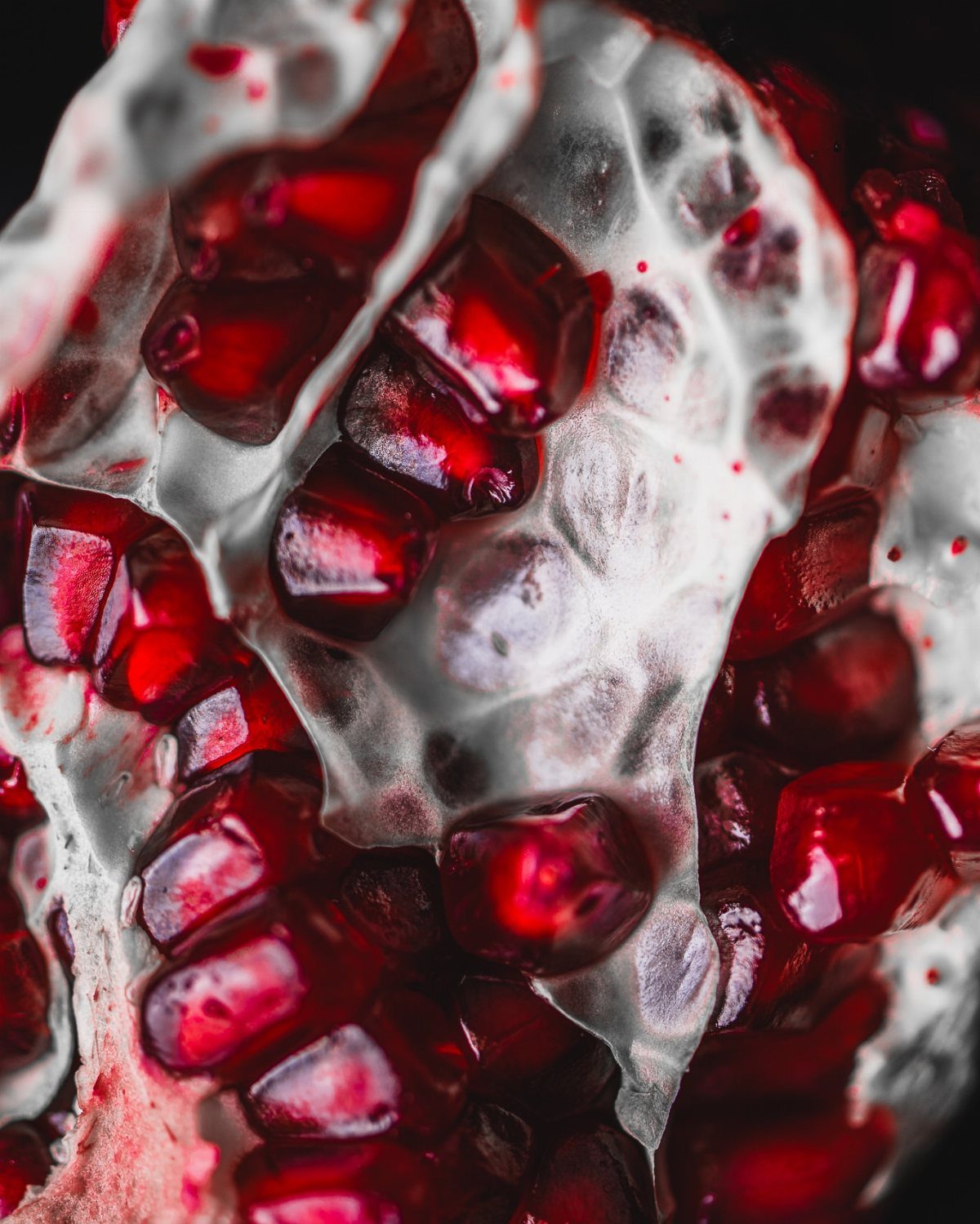 Deep red pomegranate seeds inside a white fleshy pomegranate shell.