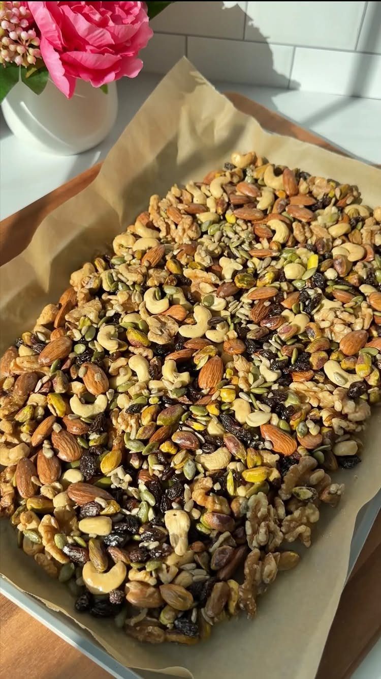 Mixed nuts and seeds on parchment paper with a pink flower in background