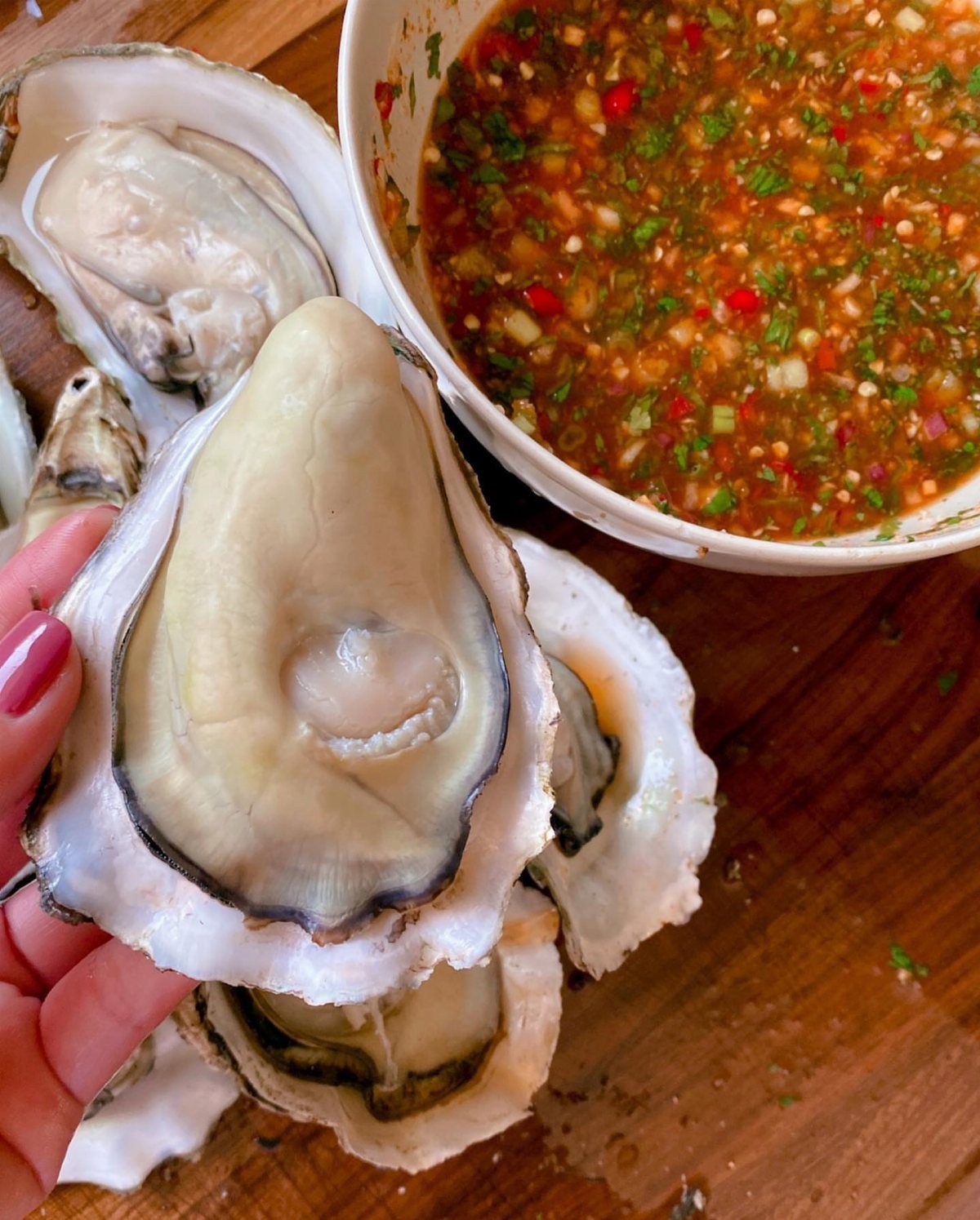 Fresh raw oysters in shells with a bowl of spicy chili dipping sauce.