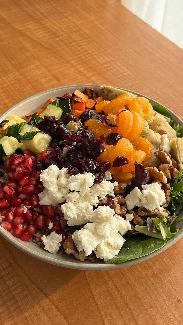 Variety bowl with pomegranate, feta, walnuts, oranges, and greens on a wooden table.