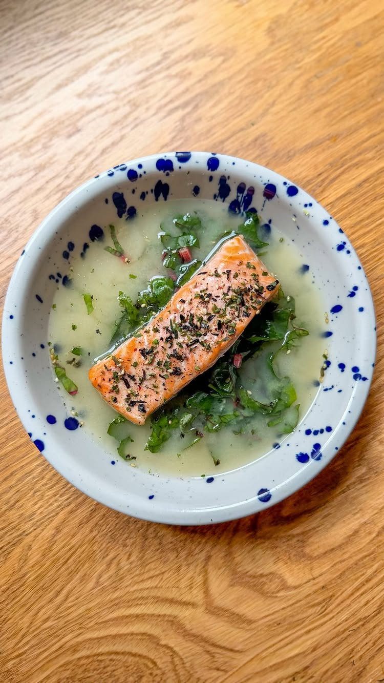 Cooked salmon fillet with herbs and greens in a creamy sauce in a bowl