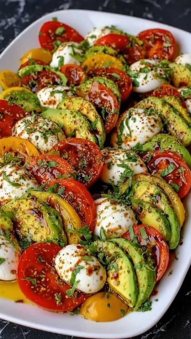 Avocado Caprese salad with tomatoes and mozzarella balls on a white platter.