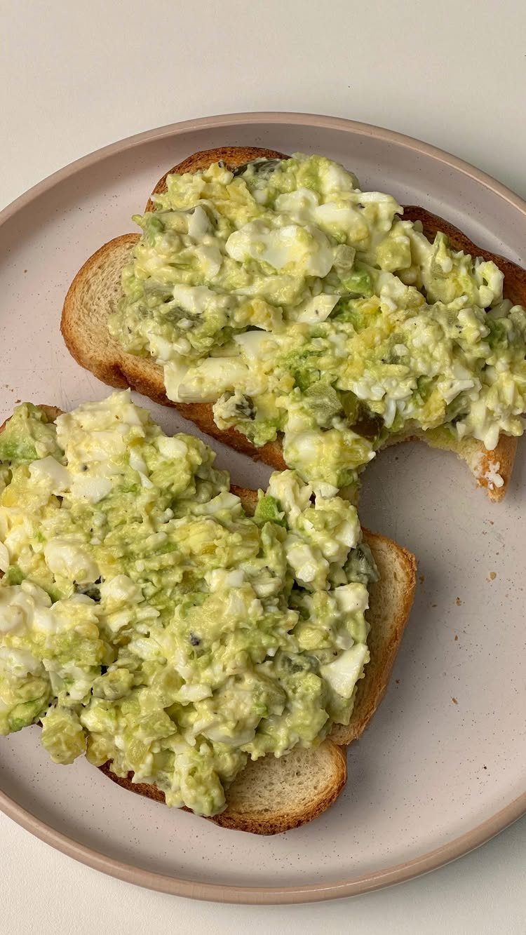 Avocado and egg salad spread on two slices of toasted bread on a plate