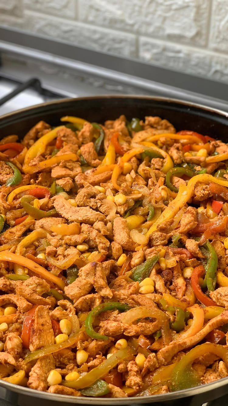 Cooked chicken with yellow and green bell peppers and corn in a pan.