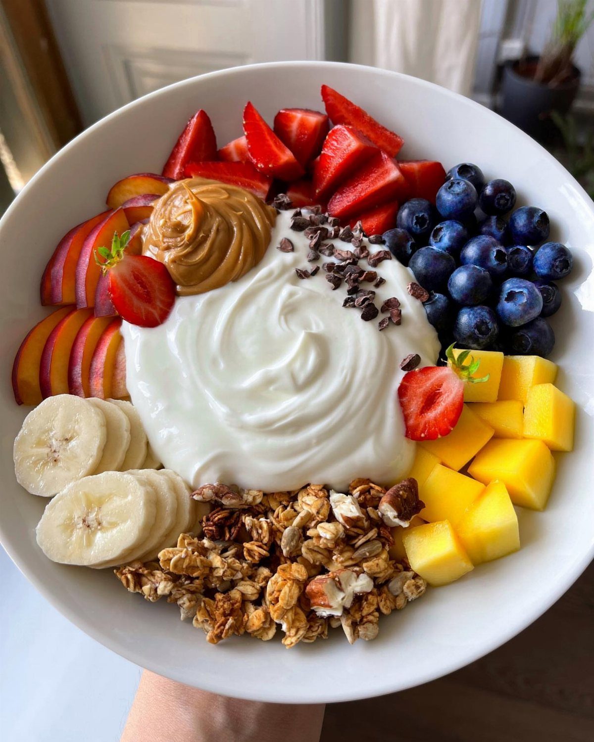 Greek yogurt bowl topped with fresh berries, mango, banana, peach, and granola.