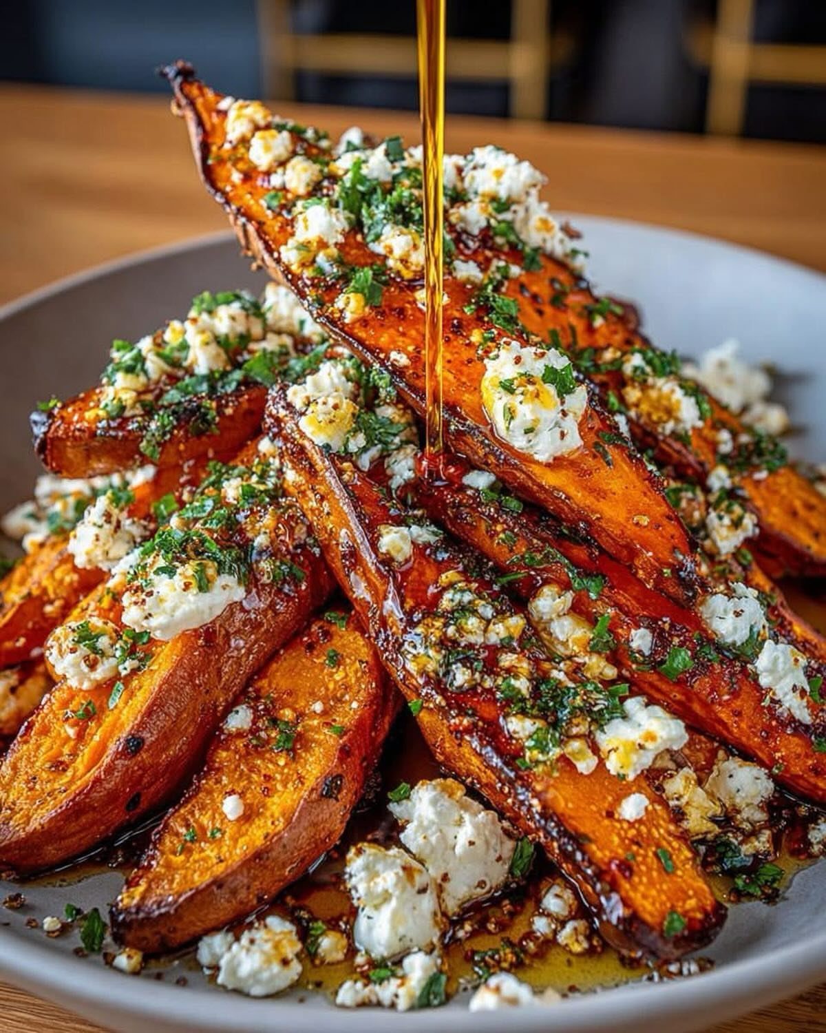 Roasted sweet potato wedges with feta cheese and herbs being drizzled with honey.
