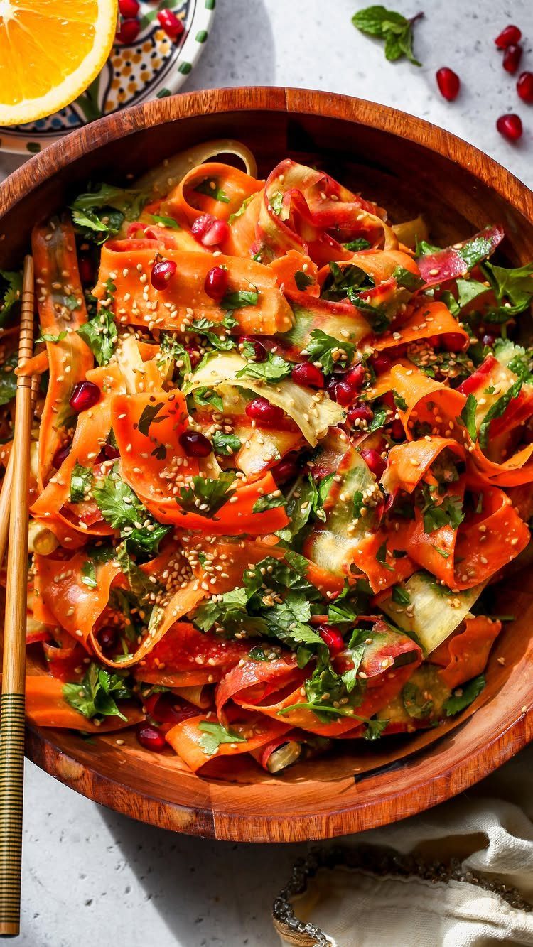 Shaved carrot salad with pomegranate seeds and sesame seeds in a wooden bowl.