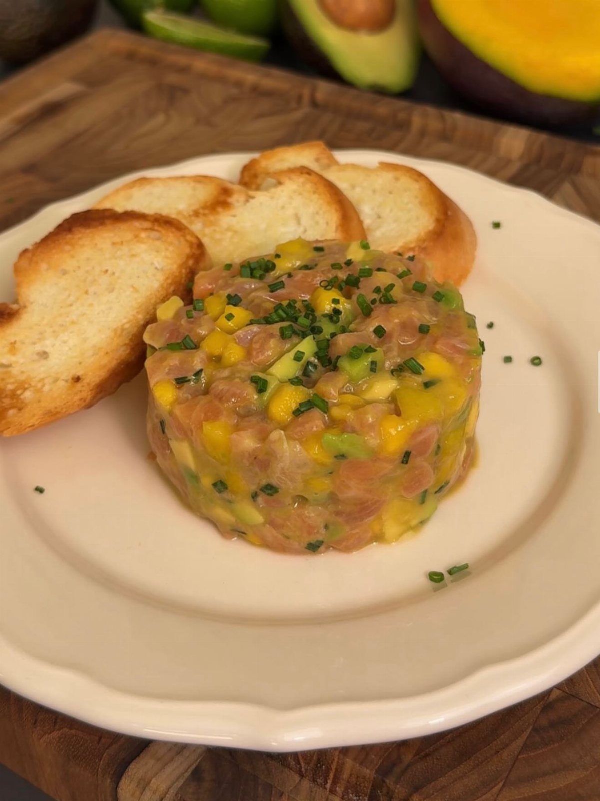 Tuna tartare with avocado and mango served with toasted baguette on a white plate.