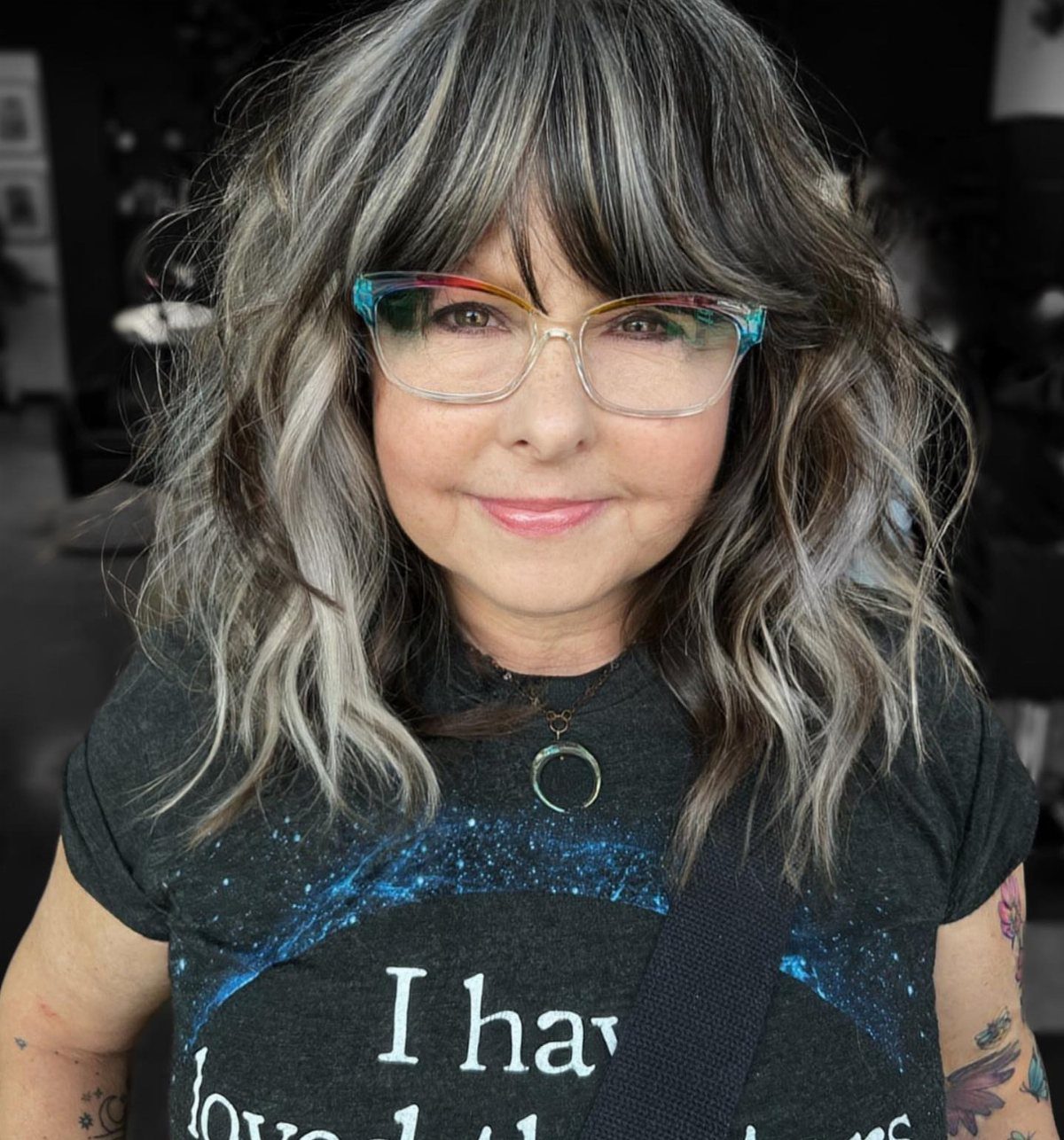 Woman with wavy gray and brown blended highlights and colorful glasses.