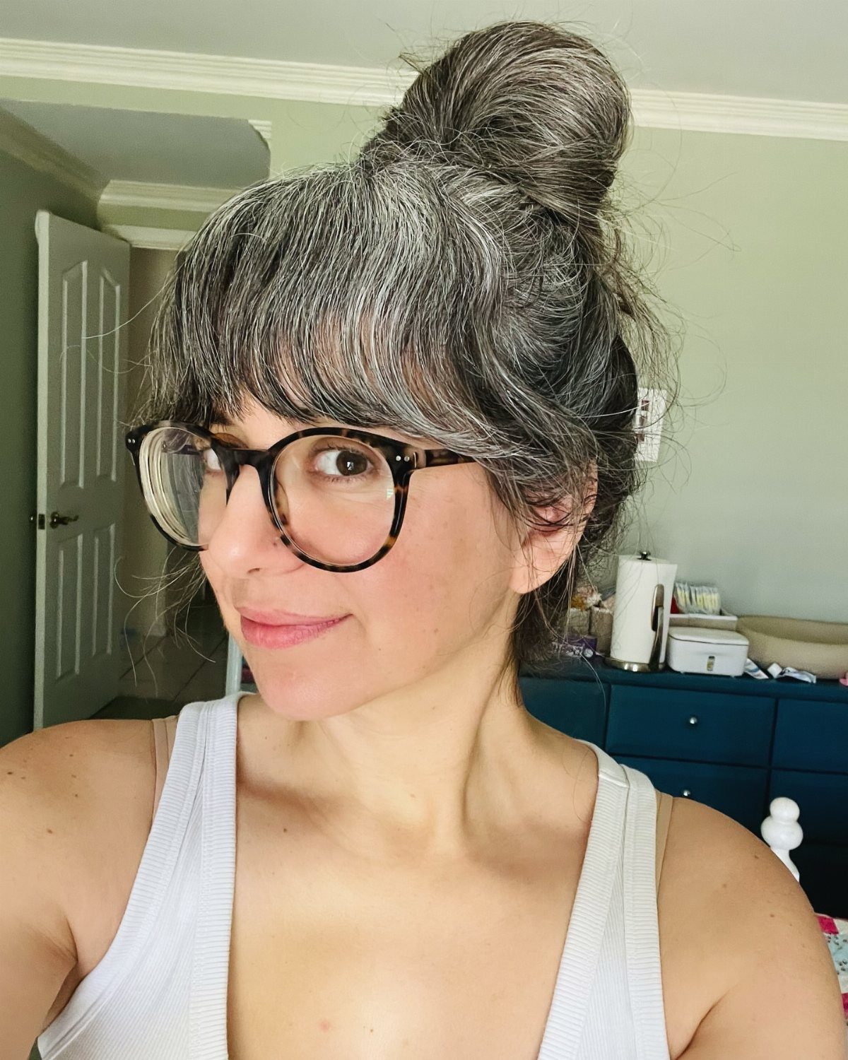 Woman with gray hair in a high bun and bangs wearing glasses.