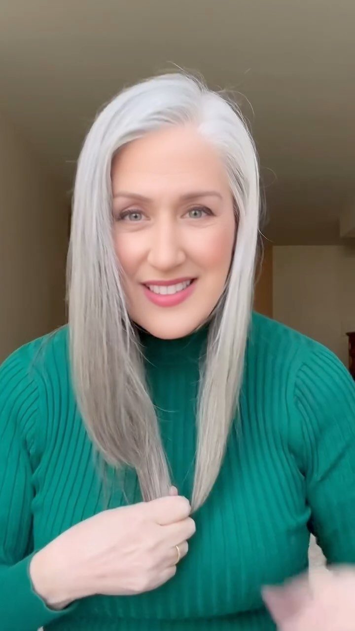 Woman with long, straight silver-gray hair wearing a green ribbed turtleneck sweater.