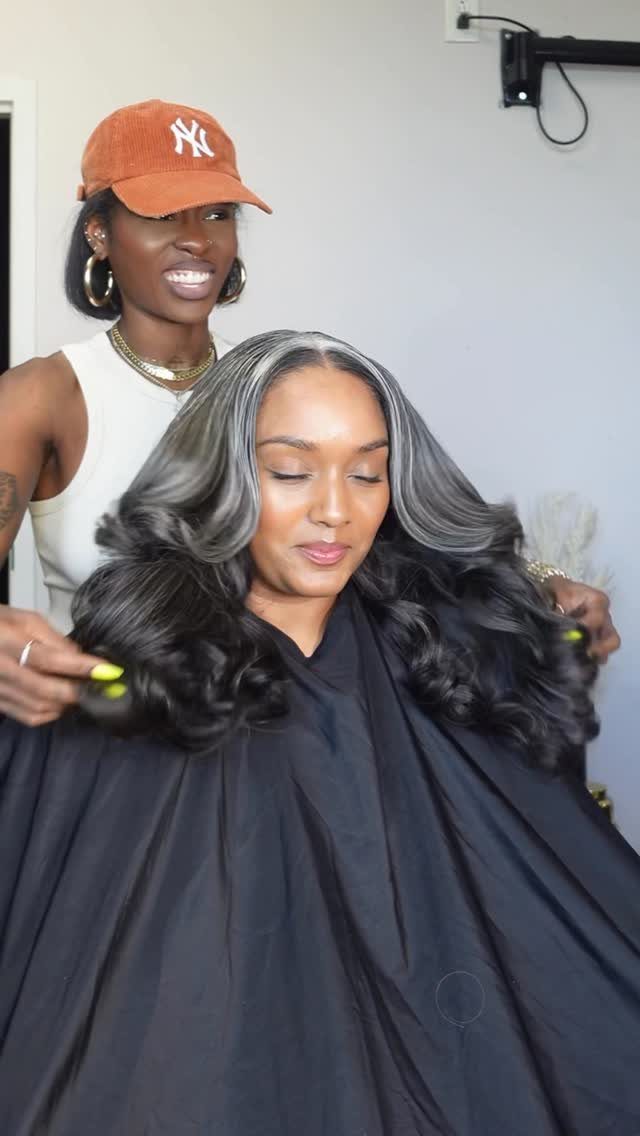 Woman with long salt and pepper wavy hair being styled by a professional.