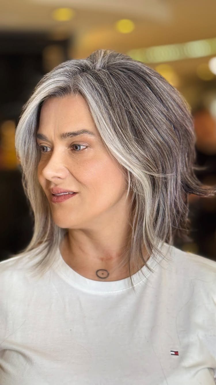 Woman with silver layered hair styled in a sweeping side-part and white t-shirt.