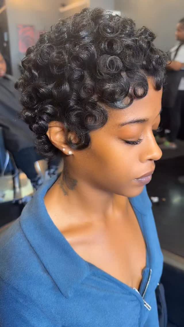 Woman with short, tightly curled black hair in a pixie grow-out style.