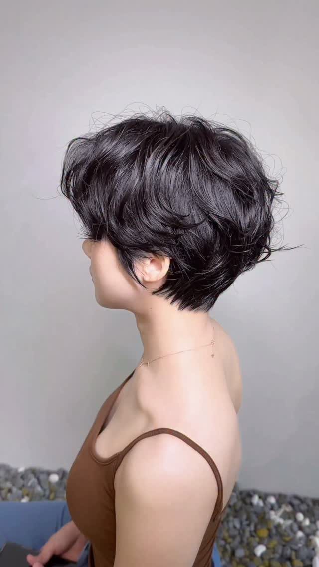 Person with a dark, layered, matte textured pixie haircut seen from the side.
