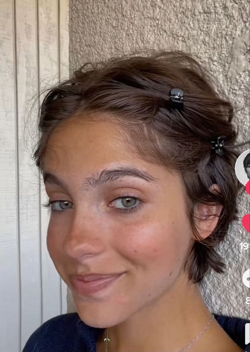 Woman with short wavy brown hair pinned back with small black hair clips.
